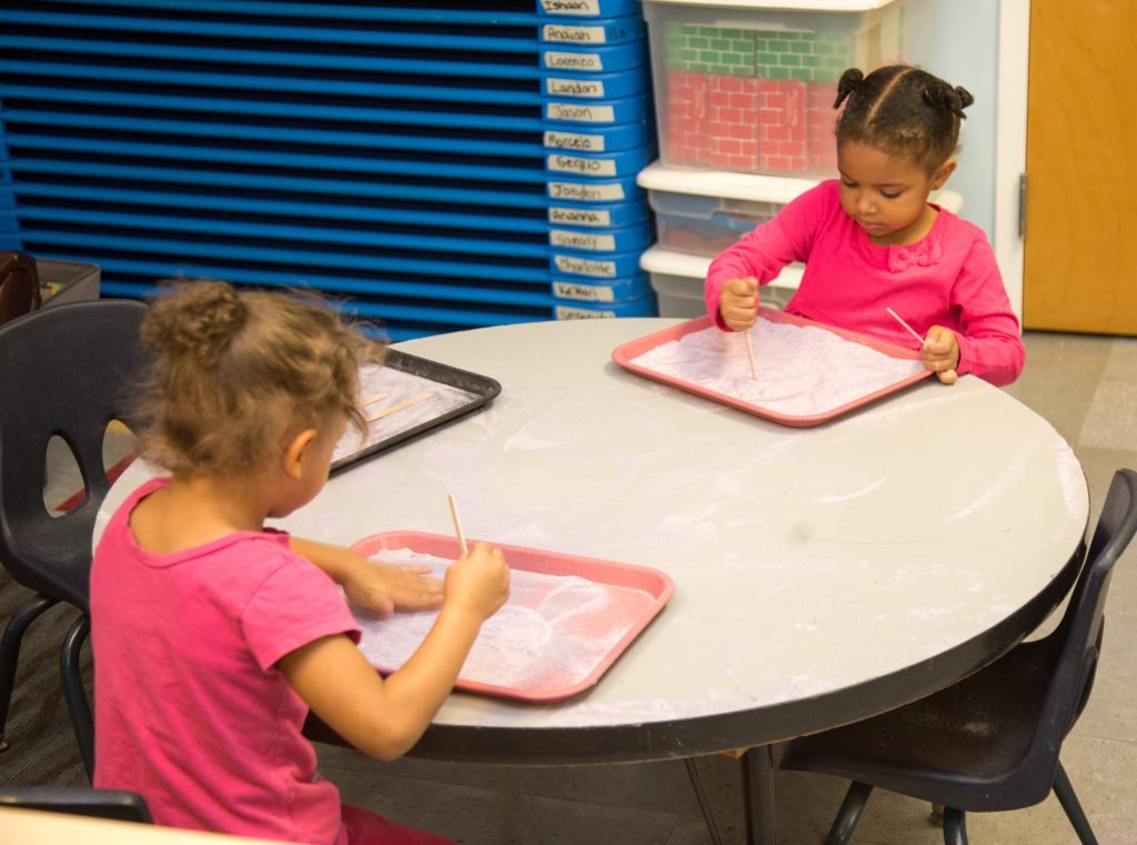 Two girls drawing at a round classroom table